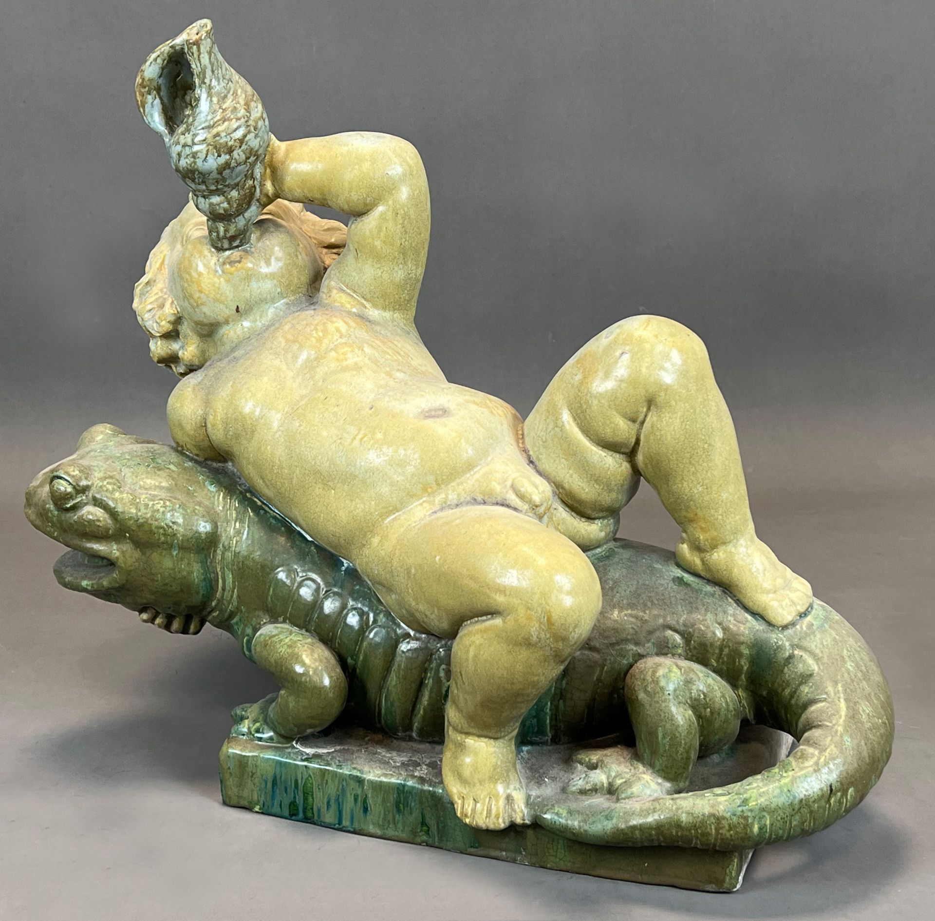 Majolica figure. Putto on a lizard. Early 20th century.