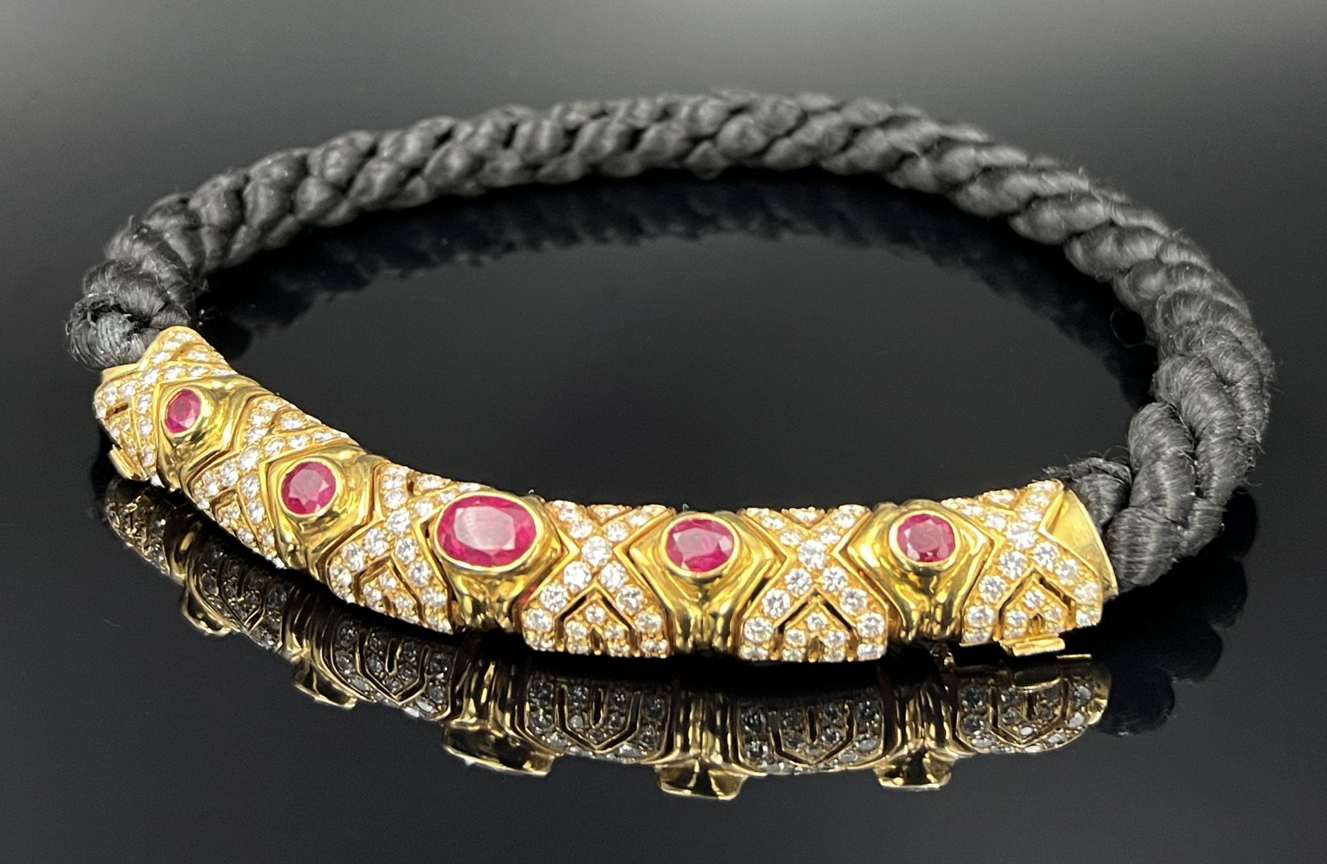 Collier. 750 Gelbgold mit üppigem Diamantbesatz, roten Farbsteinen und einem Flechtband.