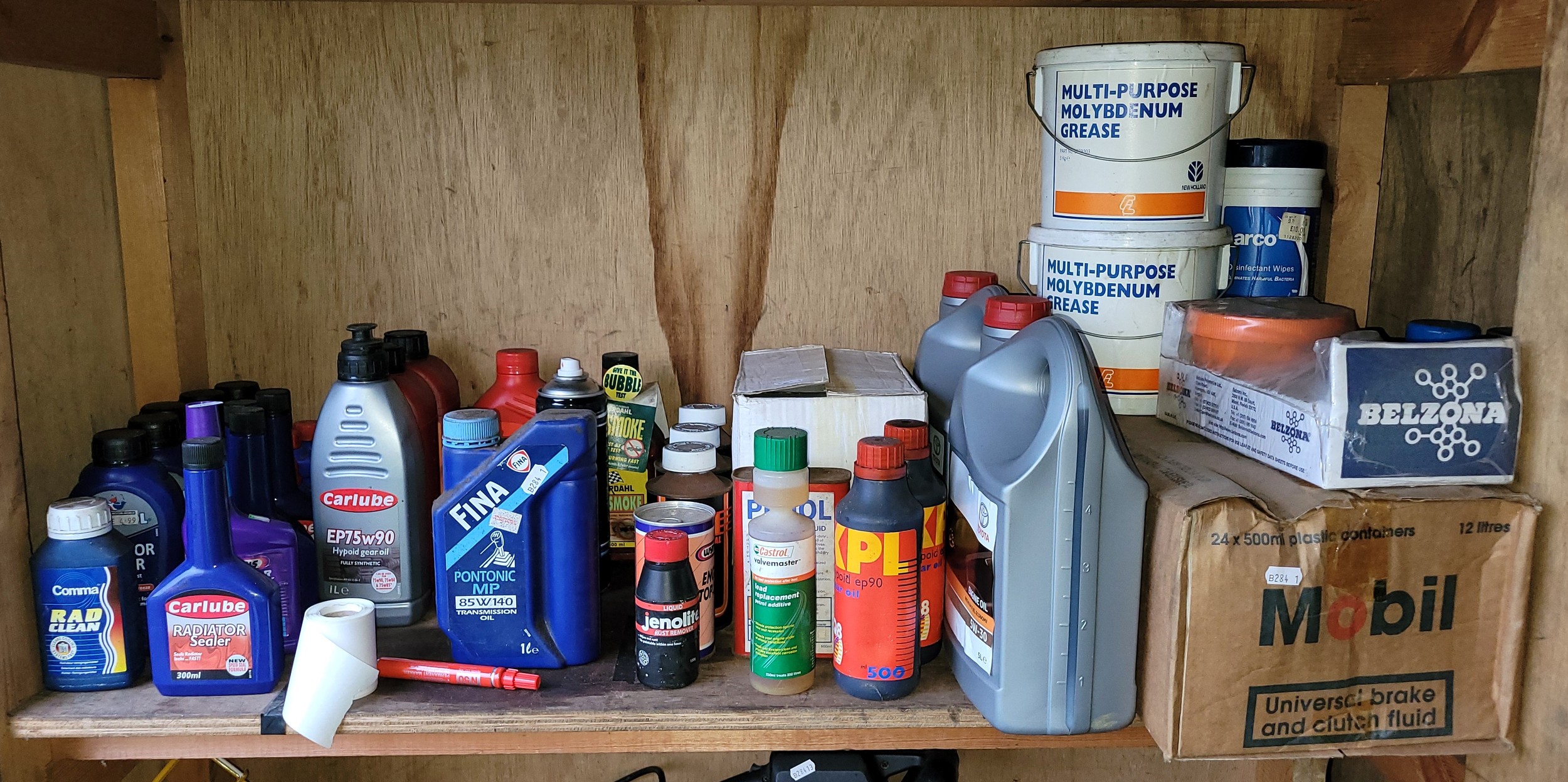 A shelf of unused motor oils and fluids to include two 5L 5W-30 engine oil bottles, Mobil break