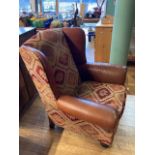 A large modern wingback armchair, upholstered in tan leather and patterned chenille fabric, with