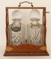 An early 20th century oak tantalus, complete with two glass decanters and plated spirit labels.