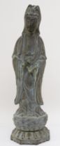 A Chinese bronze figure of Guan Yin holding a scroll weight, standing on a lotus leaf, with