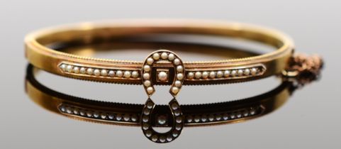 A Victorian 15ct gold horseshoe bangle, set with seed pearls, bead border and safety chain, 59mm,