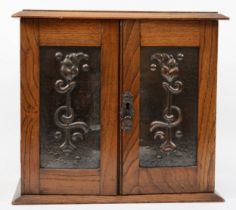 An Arts and Crafts oak and hammered copper twin door smokers cabinet, the panels decorated with
