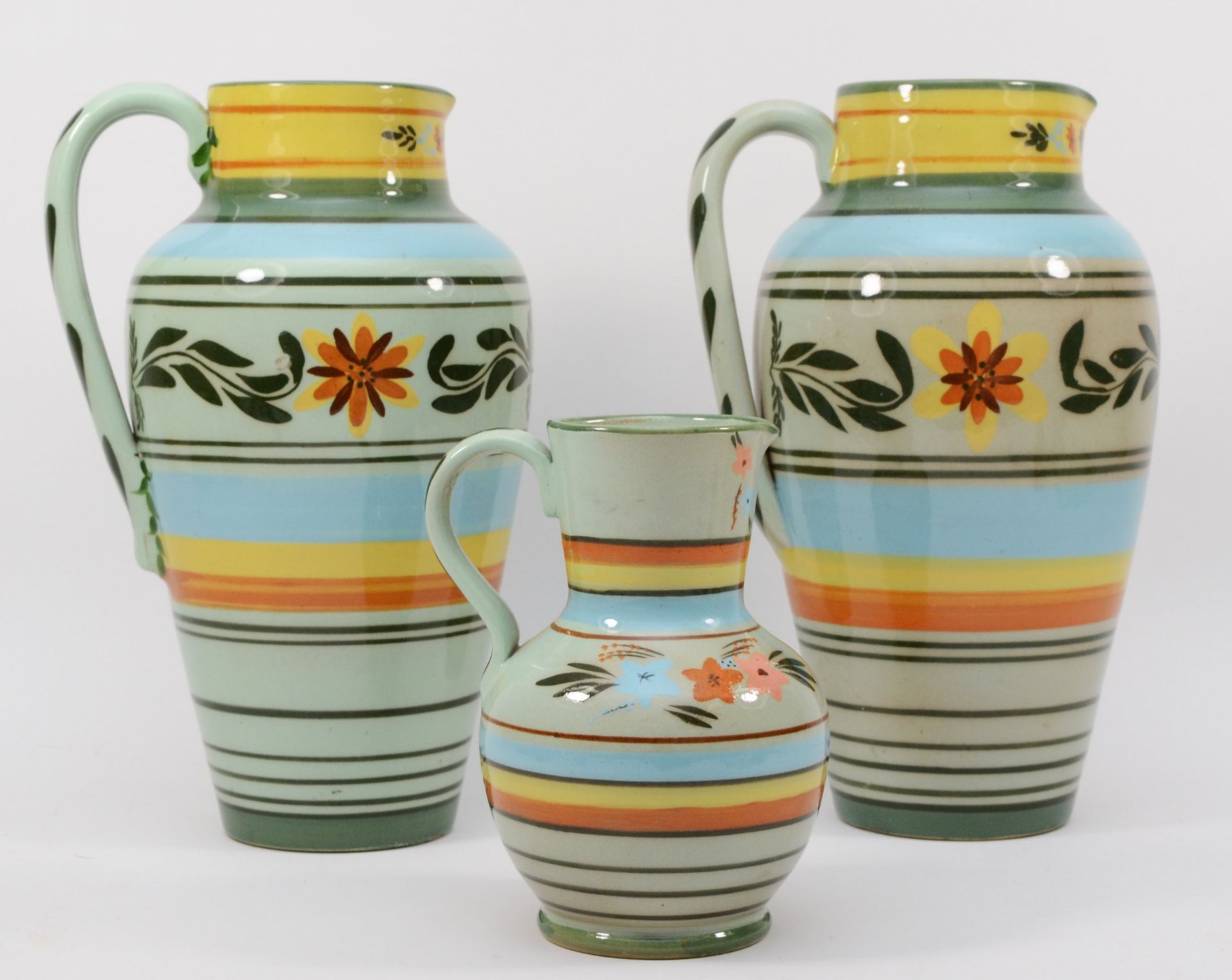 Castleford Pottery; three 20th century painted and glazed jugs decorated in the Peasant pattern,