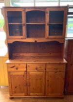 A traditional pine dresser, the rack fitted with central shelf flanked by glazed cupboards, the base