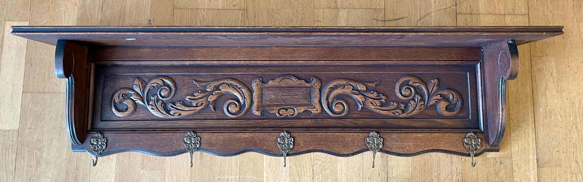 An early 20th century oak wall shelf, having carved frieze floral relief, with five brass hooks.