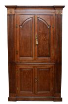 A large George III oak corner cupboard, projecting cornice over two stepped arch doors with