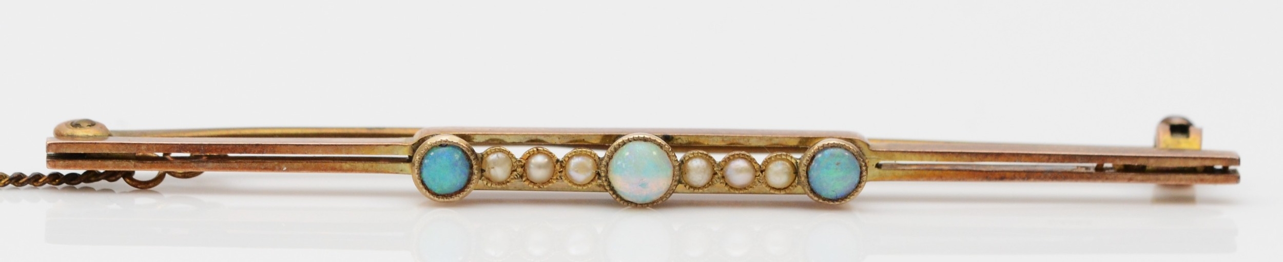 An Edwardian 9ct gold bar brooch, milligrain collet set with three opal, half pearls between,