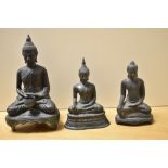 Three 19th Century Eastern cast metal seated Buddha ornaments, the largest depicting a Buddha seated