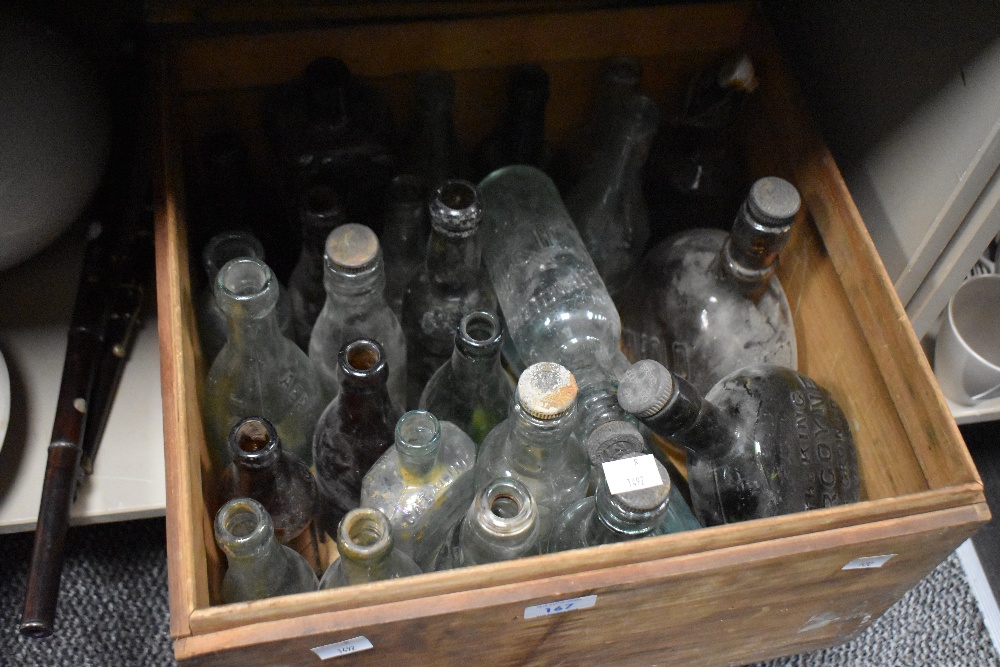 A wooden crate containing a selection of vintage and antique glass advertising bottles, including