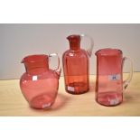 Three pieces of cranberry coloured glass, comprising tankard, and two jugs, the largest measures
