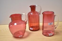 Three pieces of cranberry coloured glass, comprising tankard, and two jugs, the largest measures