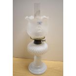 A Victorian milk glass oil lamp, with a moulded and embossed shade, measuring 55cm tall