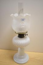 A Victorian milk glass oil lamp, with a moulded and embossed shade, measuring 55cm tall