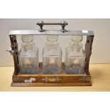 An Edwardian oak tantalus, with white metal mounts, and encasing three gut glass spirit decanters,