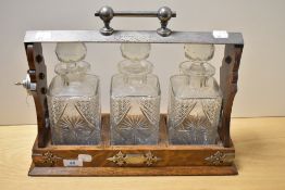 An Edwardian oak tantalus, with white metal mounts, and encasing three gut glass spirit decanters,