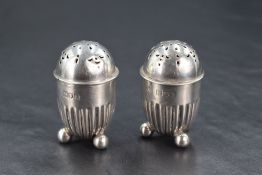 A pair of Edwardian silver condiments, of fluted bullet-form with pierced covers and three ball
