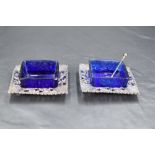 A pair of Edwardian silver and Bristol blue glass salts, of square outline with embossed and pierced
