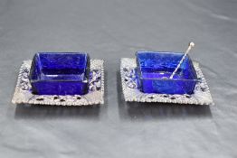 A pair of Edwardian silver and Bristol blue glass salts, of square outline with embossed and pierced