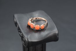 A yellow metal ring having five carved circular coral panels in collared mounts on a rose gold