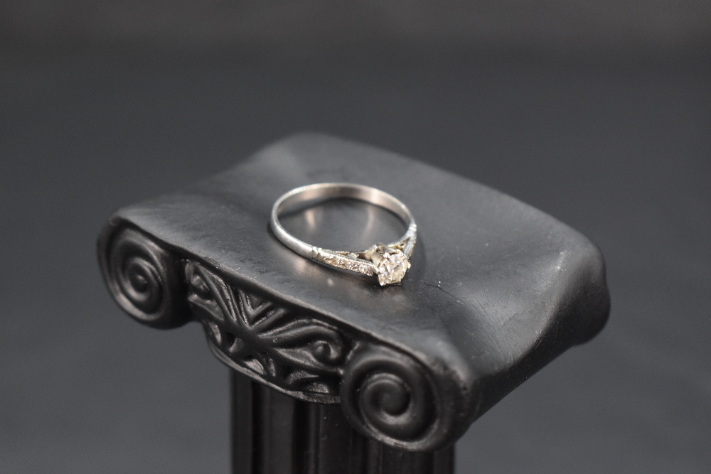 A diamond solitaire ring, approx 0.25ct in a raised claw set mount with diamond chip set shoulders