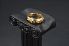 An Edwardian 18ct gold band ring having a trio of sapphire and diamond chips in star mounts within