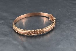 A Victorian 9ct rose gold hinged bangle having engraved decoration within a ball and wire border and