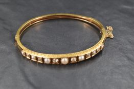 A hinged gold bangle having diamond and split pearl decoration to front panel, no marks but presumed