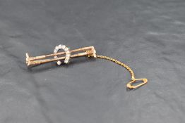 A yellow metal double riding crop brooch with central diamond set horse shoe and safety chain, no