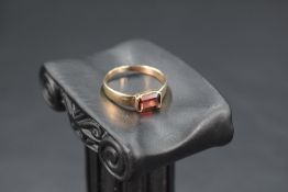 A yellow metal band ring having an inset baguette cut red/orange stone, possibly a Madeira citrine