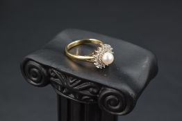 A cultured pearl ring having a double surround of diamond chips to open shoulders on a 9ct gold
