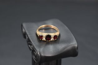 A garnet trio ring interspersed by white stones, possibly sapphires in a moulded gallery mount on