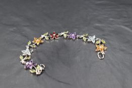 A multi gem bracelet in the form of a string of flowers in a silver mount, gems include amethyst,