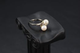 A cultured pearl crossover ring with sapphire chip set shoulders on a white metal loop stamped