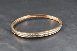 A 9ct gold hinged bangle having a double row of diamond chip decoration to one half and a