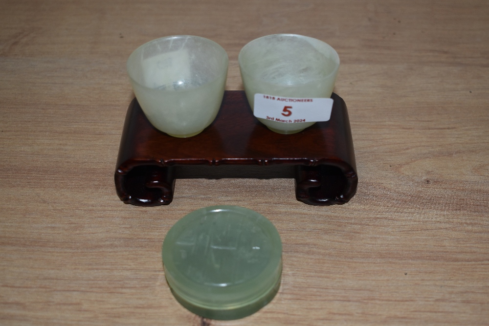 Two Chinese jade Mijiu cups and lidded trinket box with hardwood stand