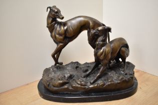 A reproduction cast and patinated metal study of two playful greyhounds on a naturalistic base and