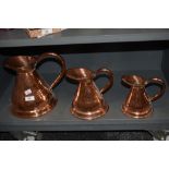 Three Victorian planished copper pitchers, of graduating sizes, the largest measures 26cm tall