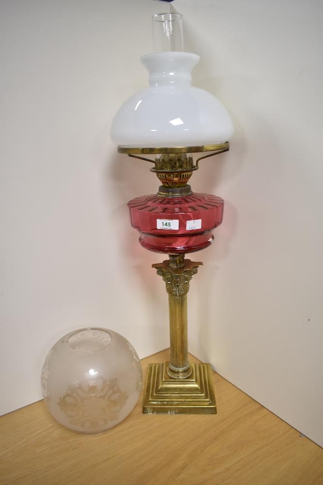 An early century brass and cranberry glass oil lamp, of Corinthian column form with stepped square