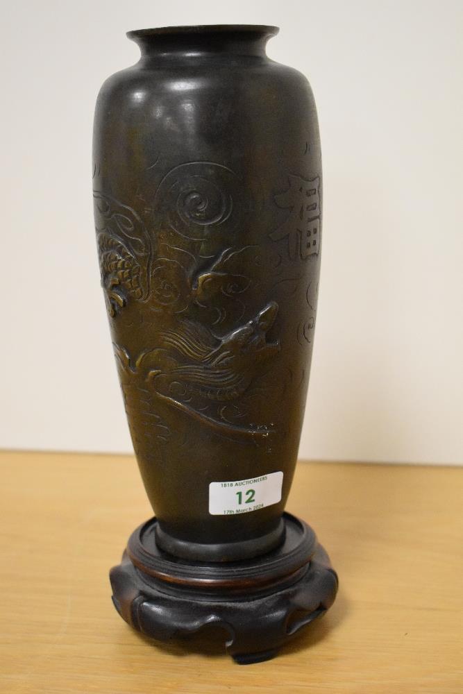 A 19th Century Chinese bronze metal vase, decorated in relief with a dragon, raised on a hardwood