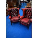 A pair of red leather button back wing armchairs