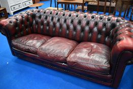 A traditional oxblood leather chesterfield three seater settee and similar chair