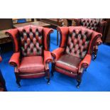 A pair of red leather button back wing armchairs