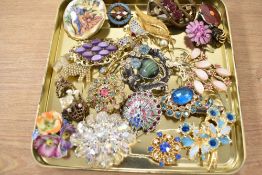 An assortment of costume brooches, to include floral bouquet examples and a paste set peacock.