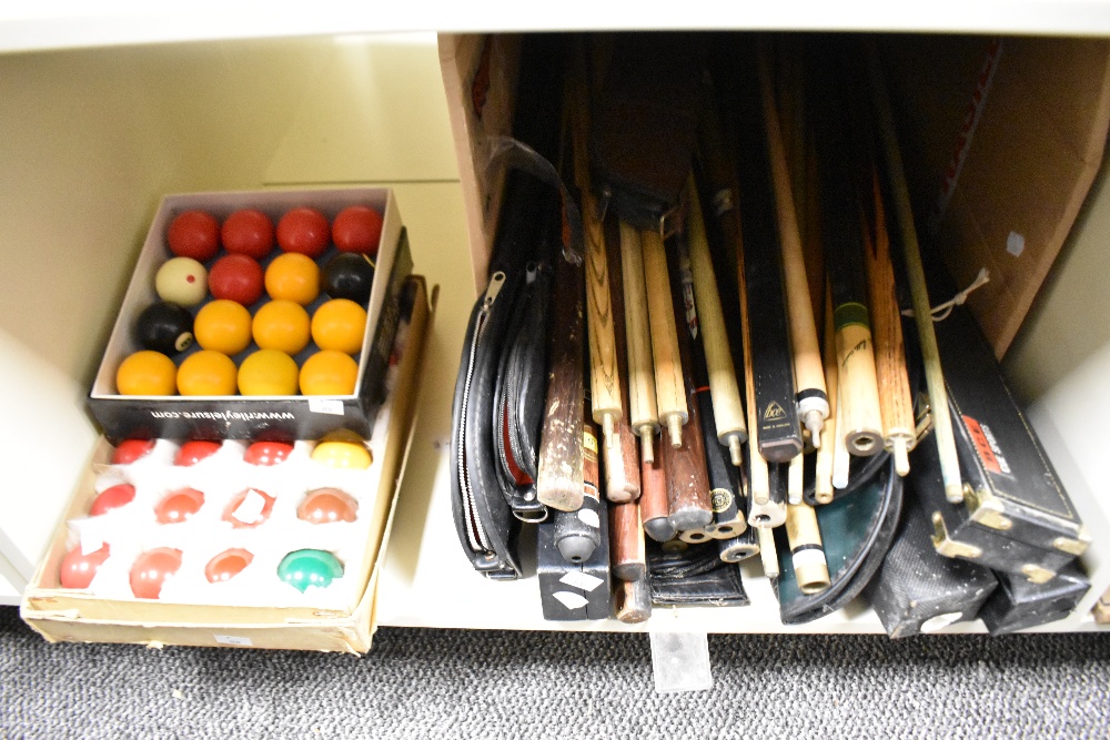 A collection of pool / snooker balls in boxes and a large amount of cues and some cases.