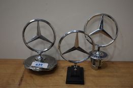 Three Mercedes car mascots, one on cap, one on mount and one off car