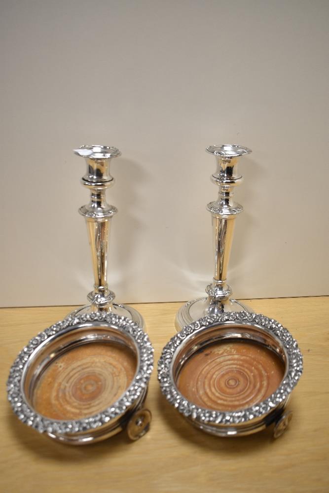 A pair of silver plated candlesticks and two unusual champagne or spirit coasters, having later