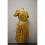 A 1950s floral day dress in yellow hues, with original belt, heart shaped patch pocket to front