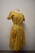 A 1950s floral day dress in yellow hues, with original belt, heart shaped patch pocket to front